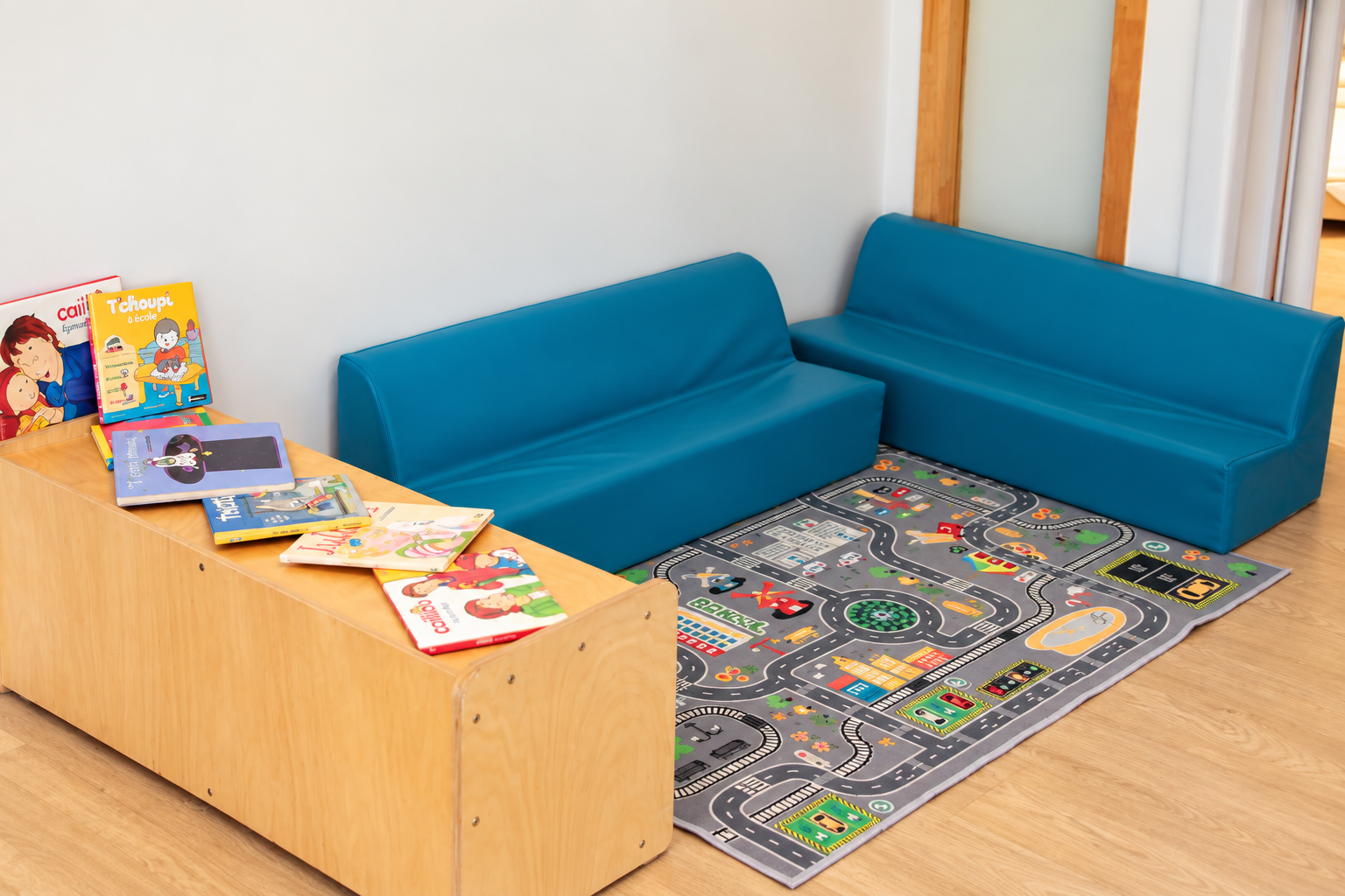 Coin lecture aménagé avec banquettes bleues, livres et tapis de jeu